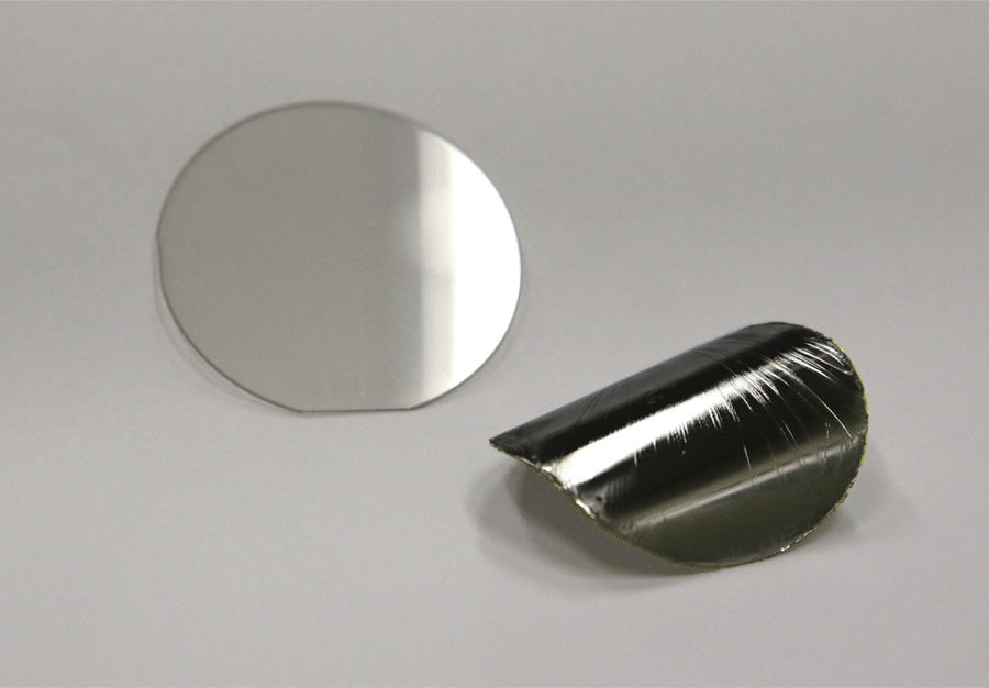 This image shows a thick bulk gallium nitride (GaN) crystal wafer (2 inches in diameter) with a GaN film in the foreground fabricated by controlled spalling (its film thickness is ~20 microns or 1/5th the thickness of a sheet of paper. 1Credit: Bedell/IBM Research
