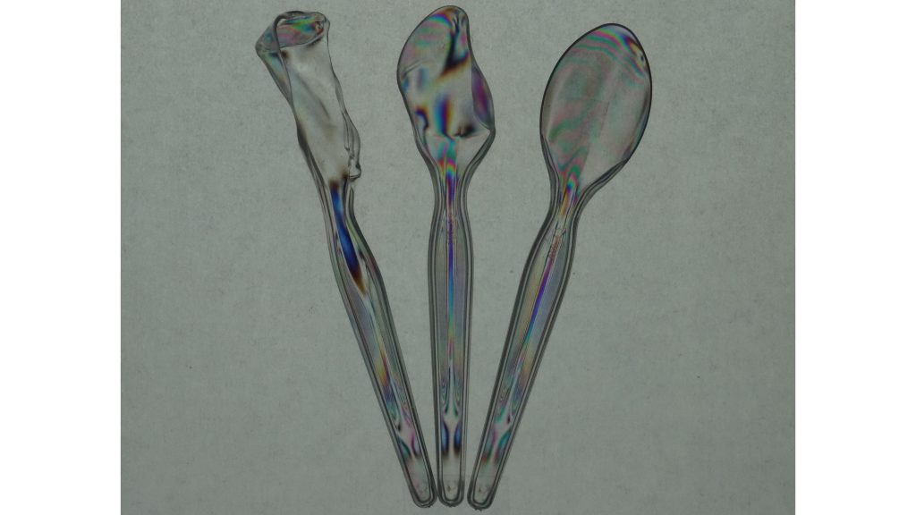 The stochastic stress-induced birefringence within plastic spoons left in the hot sun is visualized through polarization-filtered coloration. The spoons are placed between a pair of co-aligned polarizer sheets in an open-gate arrangement, with a backing of parchment paper to act as a diffuser for sunlight illumination. CREDIT: Aaron Slepkov, Trent University