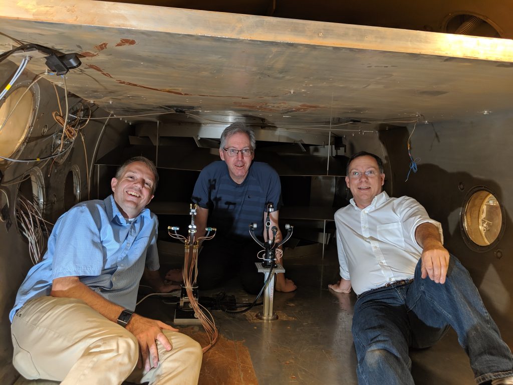 Authors Robert White (left), Ian Neeson (center), and Don Banfield (right) in the Mars Simulation Wind Tunnel at Aarhus University, Denmark, in 2019, preparing to test early prototypes of the Mars acoustic anemometer, seen in the center. The two prototypes were manufactured by Tufts University (left) and VN Instruments (right). Image credit: White, Neeson, and Banfield