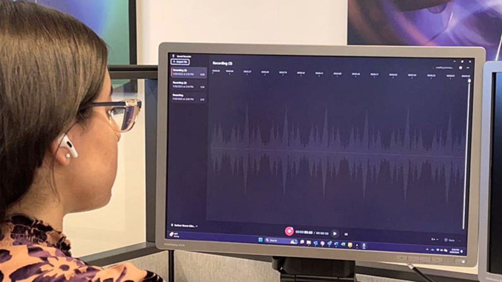 Woman wearing glasses looking at a computer screen that is showing an acoustical recording graph.