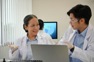 Senior scientist mentoring a younger colleague during a research discussion over a laptop