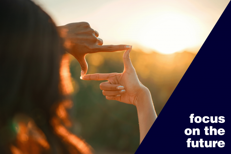 Person framing the sunrise with their hands beside a graphic banner saying, 'focus on the future'.