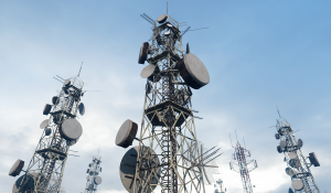 Telecommunications towers with interconnected antenna systems reaching upward against a bright blue sky.