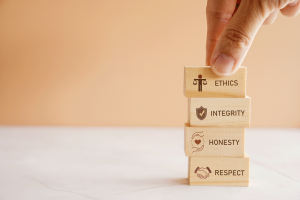 Four stacked wooden blocks displaying ethics, integrity, honesty, and respect, with a hand positioning the top block.