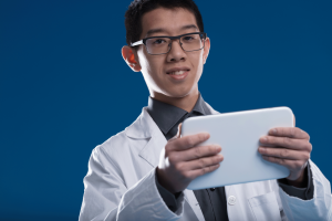 Young scientific researcher wearing glasses and a lab coat using a handheld digital tablet.